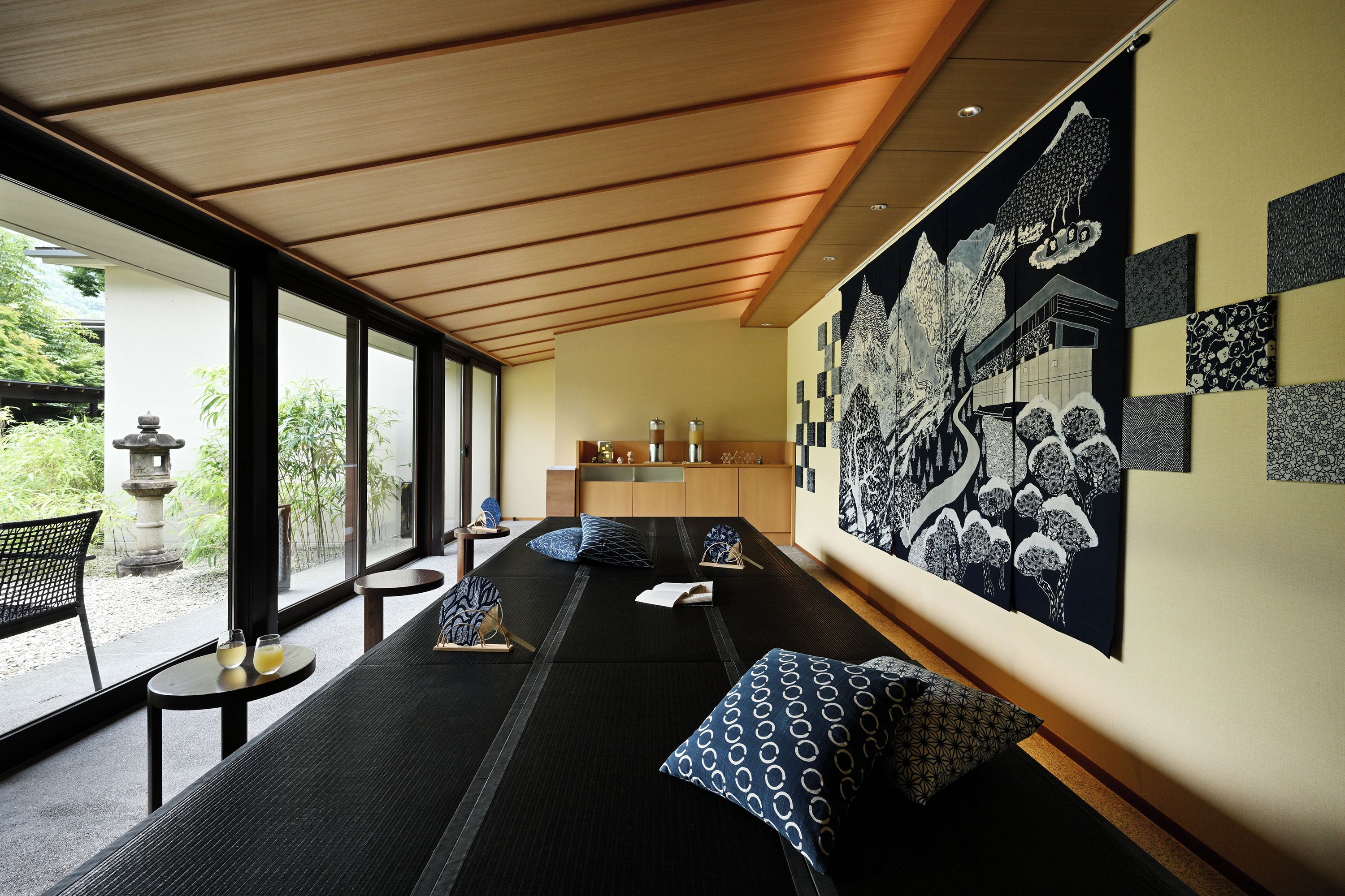 A modern room with a long bed, a small table, and a large wall with various black and white patterns.