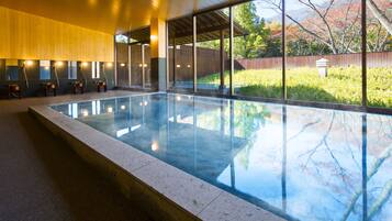 A modern indoor swimming pool with a clear view of the outdoors, wooden panel walls, and a tiled floor.