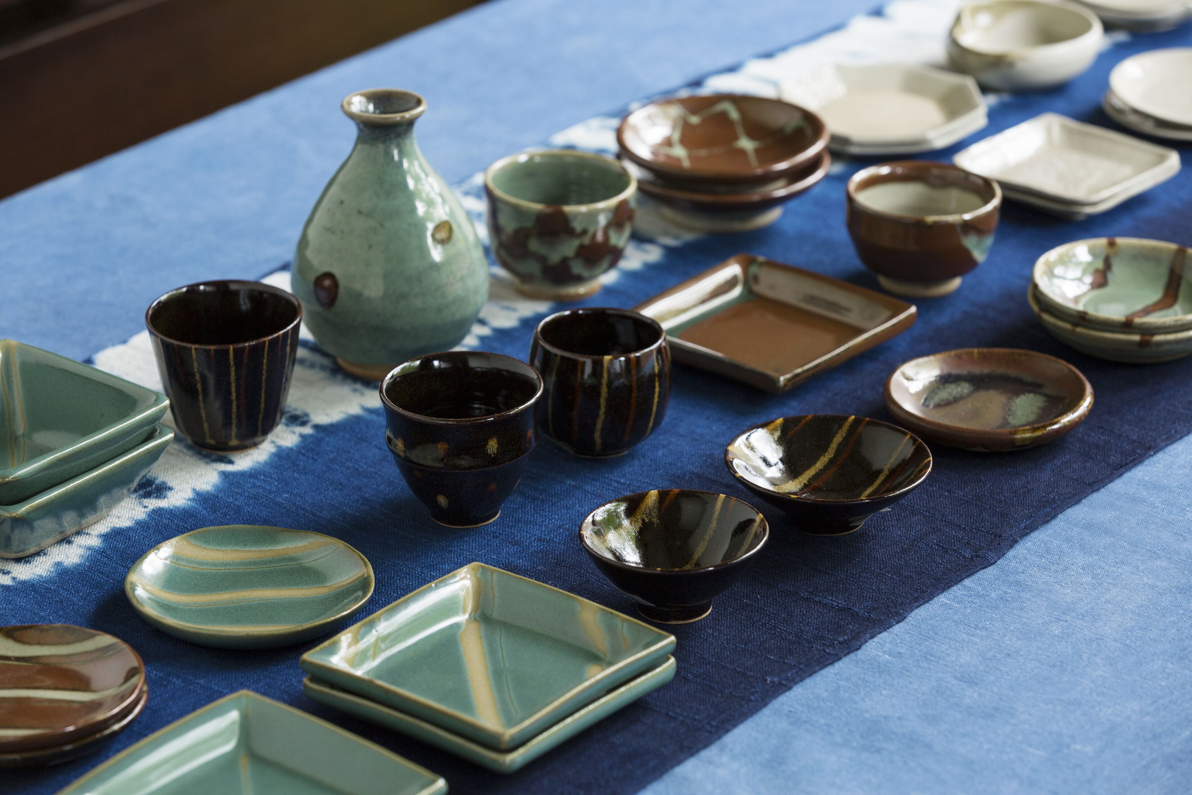 A variety of ceramic dishes and bowls arranged on a table with a blue cloth.