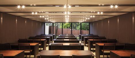 Un comedor amplio con varias mesas y sillas, un techo alto con iluminación empotrada y ventanas grandes que ofrecen vistas al exterior.