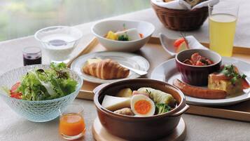 A breakfast setting with various dishes, including a salad, soup, croissant, and a glass of juice.