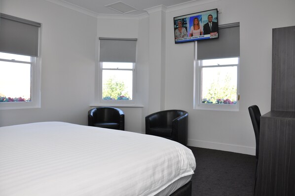 A hotel room with a large bed, two black chairs, a desk, and a TV on the wall. - Queens Head Hotel (North Hobart)