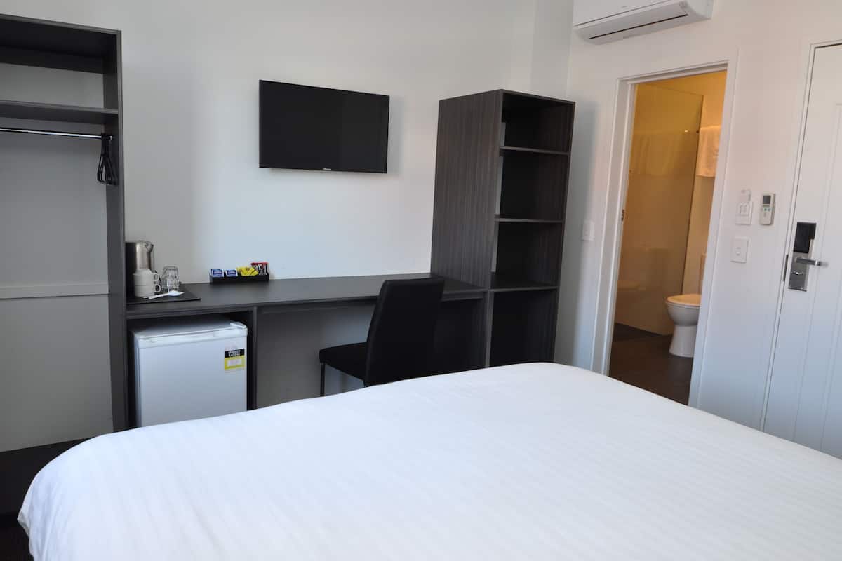 A hotel room with a bed, a desk with a chair, a television, a mini-fridge, and a wardrobe.