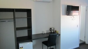 A compact room with a kitchenette, a TV mounted on the wall, and a chair. - Queens Head Hotel (North Hobart)