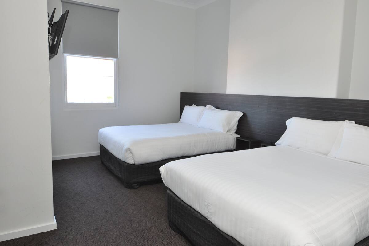 A hotel room with two single beds, a large window, and a dark headboard.