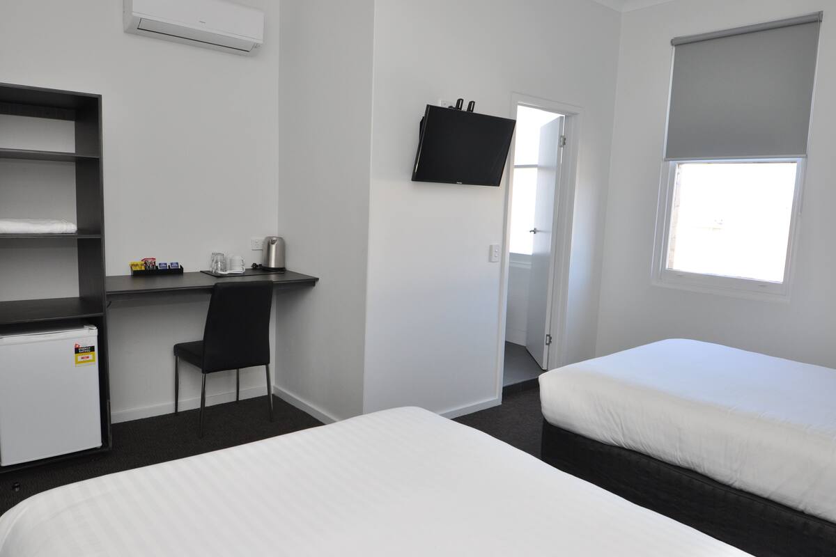A hotel room with a bed, a desk with a chair, a television, and a window.