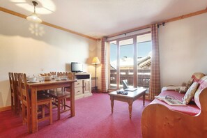 A cozy room with a dining table, chairs, a sofa, a TV, and a window with a view.