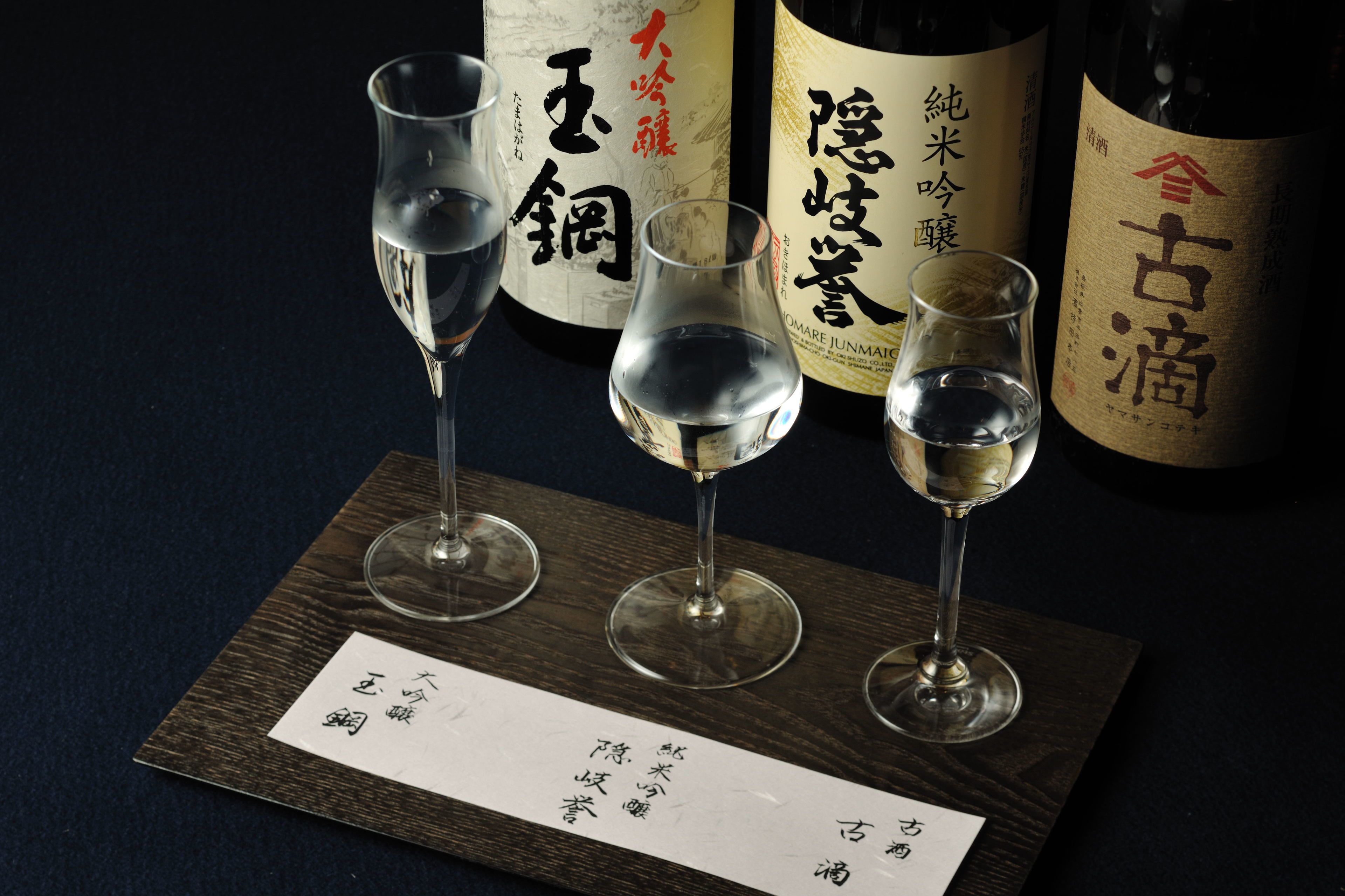 Three wine glasses on a wooden tray with labels and a menu.