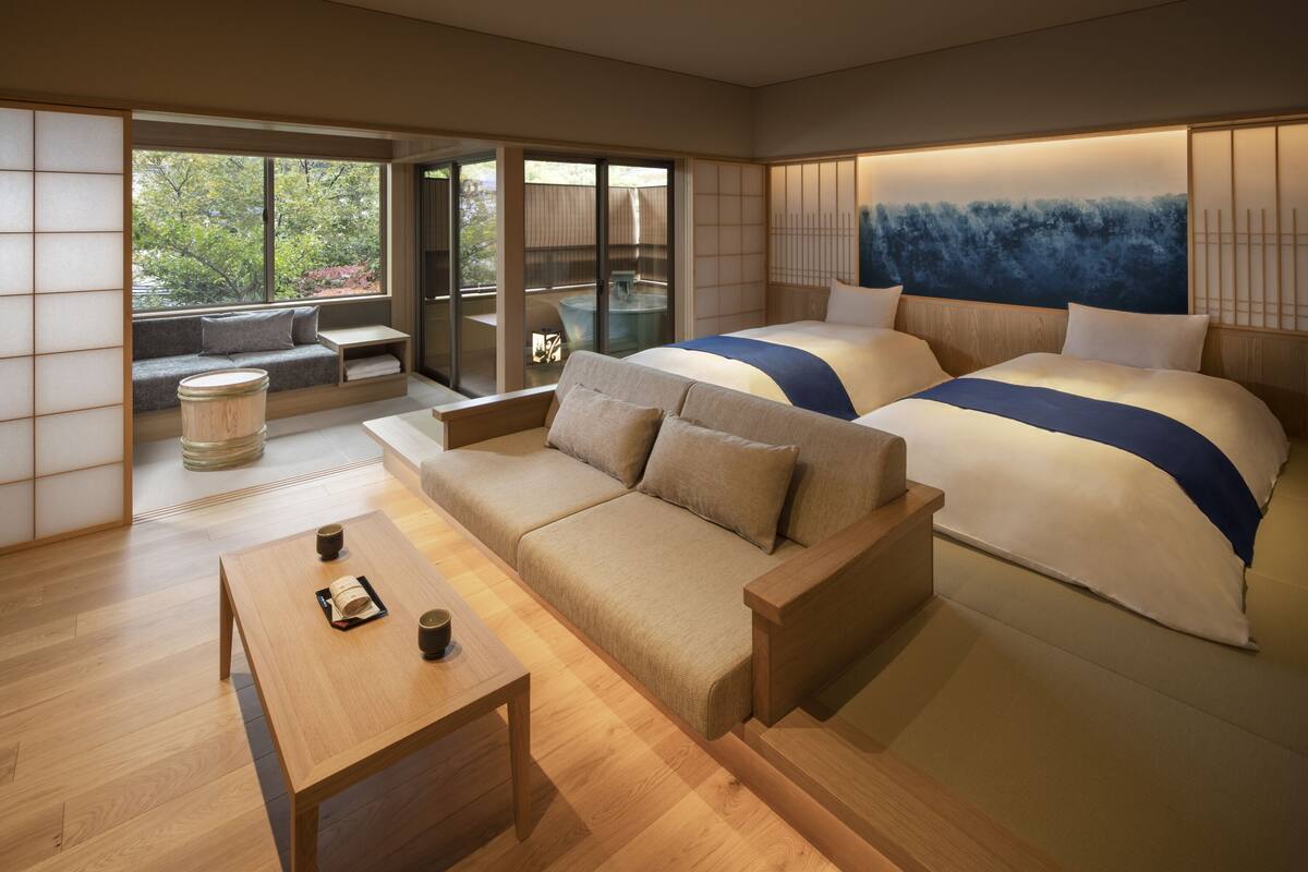 Une chambre d’hôtel moderne, dotée d’un canapé, de deux lits, d’une table basse en bois et offrant une vue sur un balcon extérieur accessible par une porte coulissante.