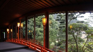 Pasillo con techo de madera y vista a un jardín con un puente rojo y faroles.