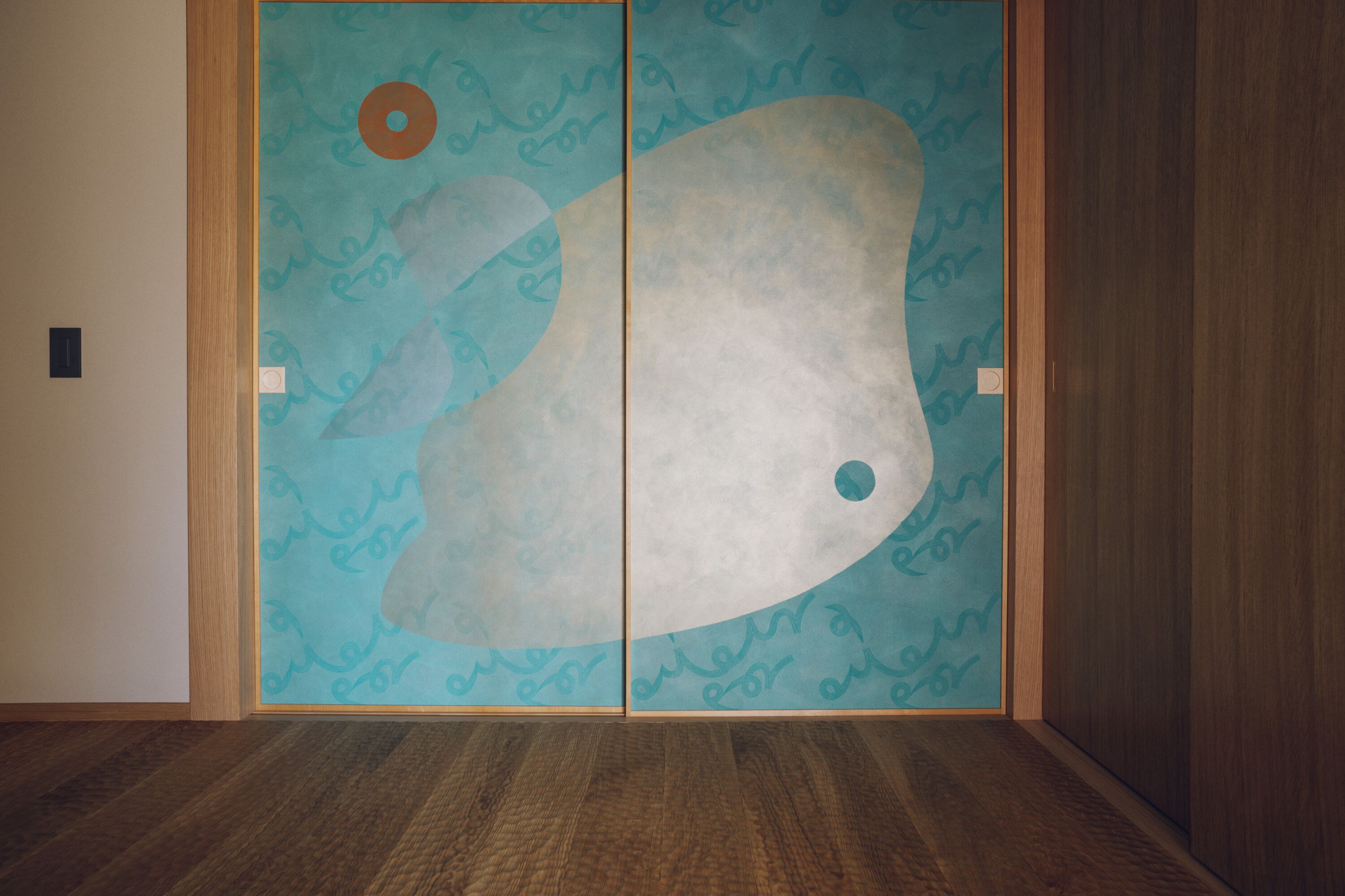 A room with a wooden floor and a sliding door with a blue and white abstract design.