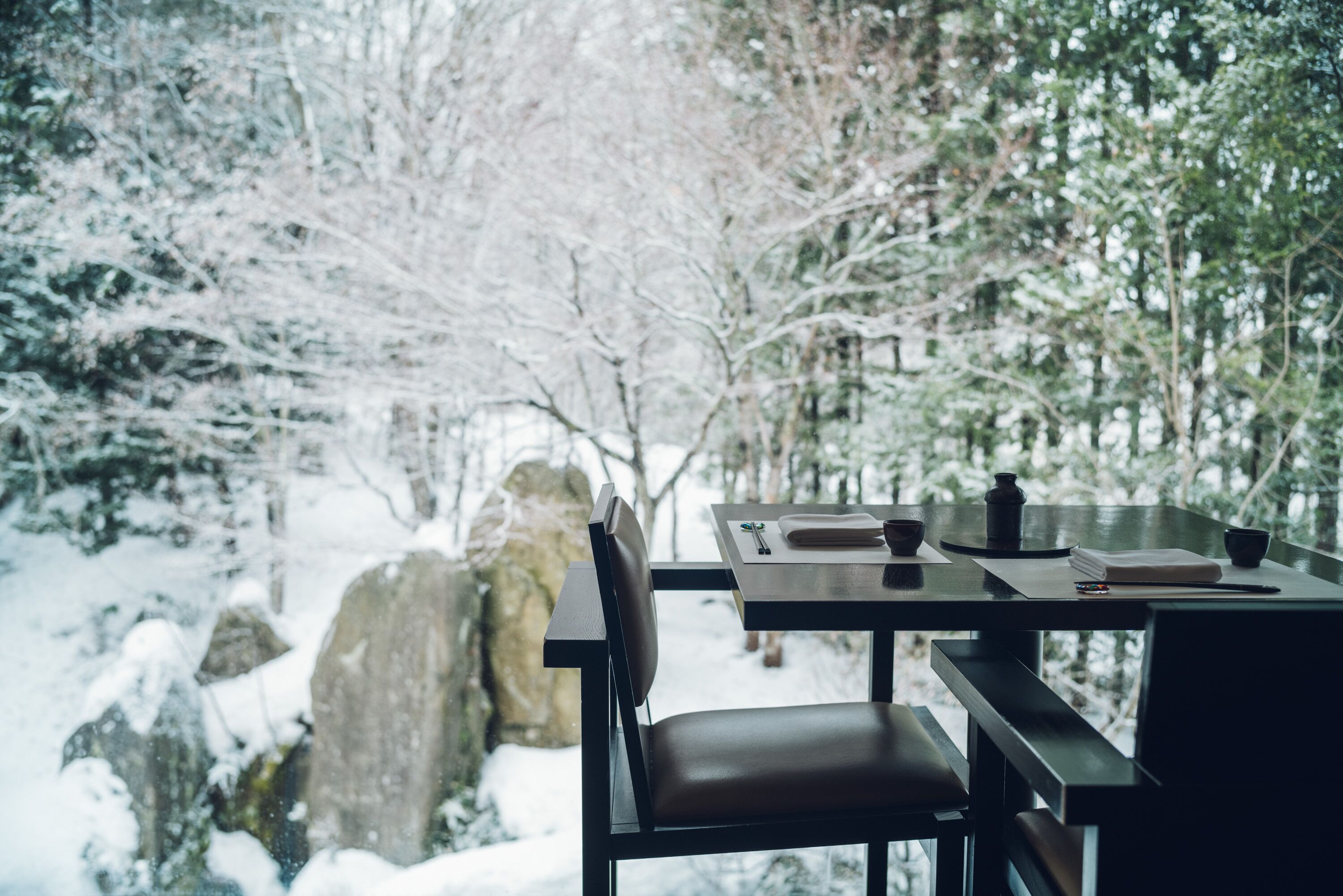 A table with a chair, a book, and a cup in a snowy outdoor setting.