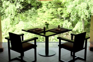 Ein moderner Esstisch mit zwei Stühlen, einer Blumenvase und Blick auf einen üppigen, grünen Wald durch ein Fenster.