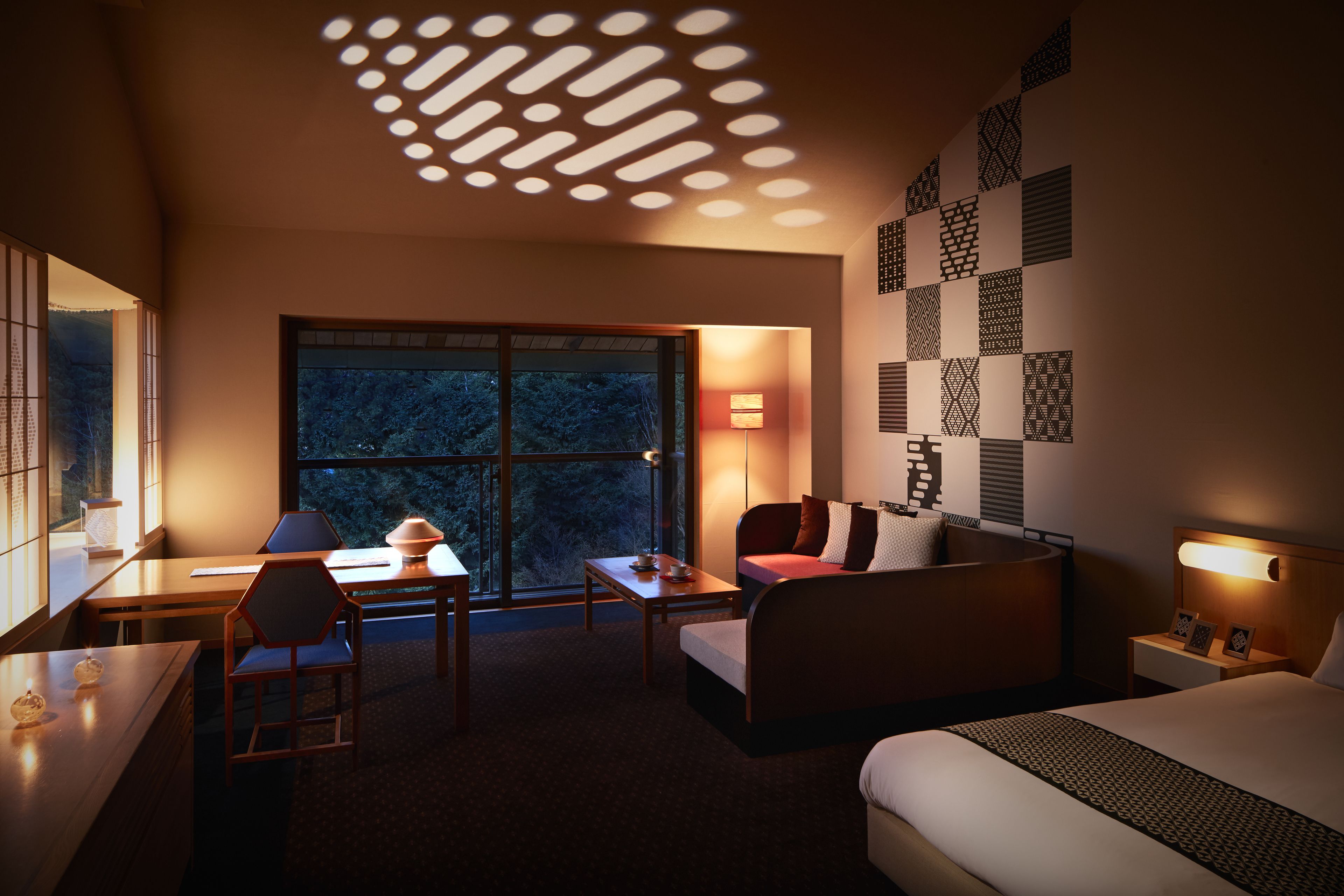 A hotel room with a large window, a desk, a chair, a sofa, and a bed.