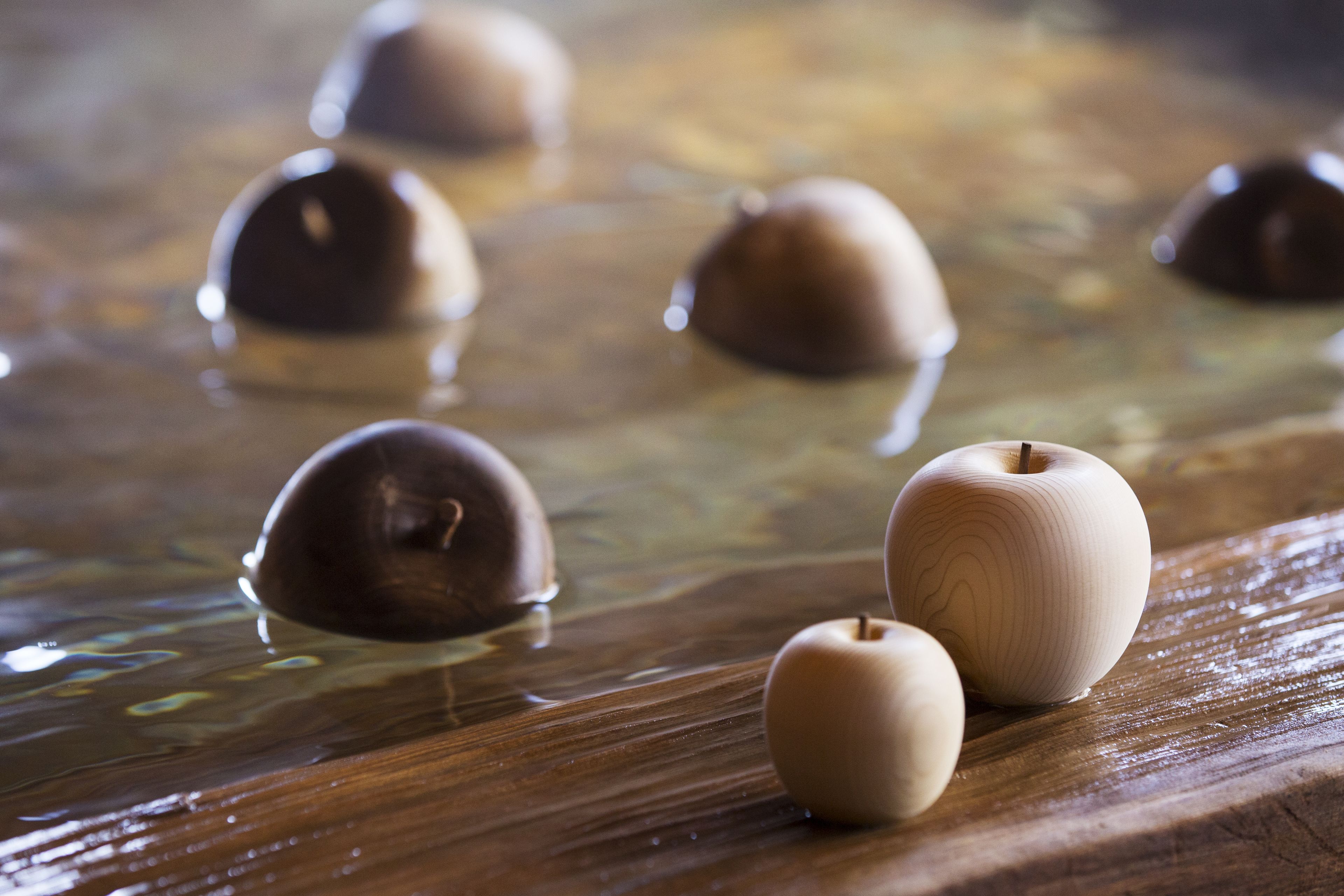 A wooden surface with several spherical objects, possibly made of chocolate, in a liquid.