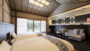 A hotel room with two beds, a sofa, a TV, and a large window with a view of trees.