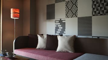 A modern hotel room with a sofa, pillows, a table with cups, and a patterned wall.