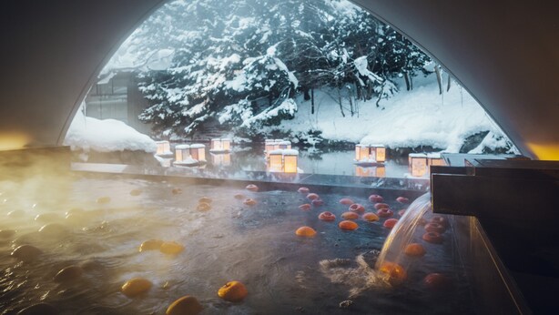 Tinaja con bombas de baño anaranjadas, rodeada de árboles cubiertos de nieve y faroles iluminados.