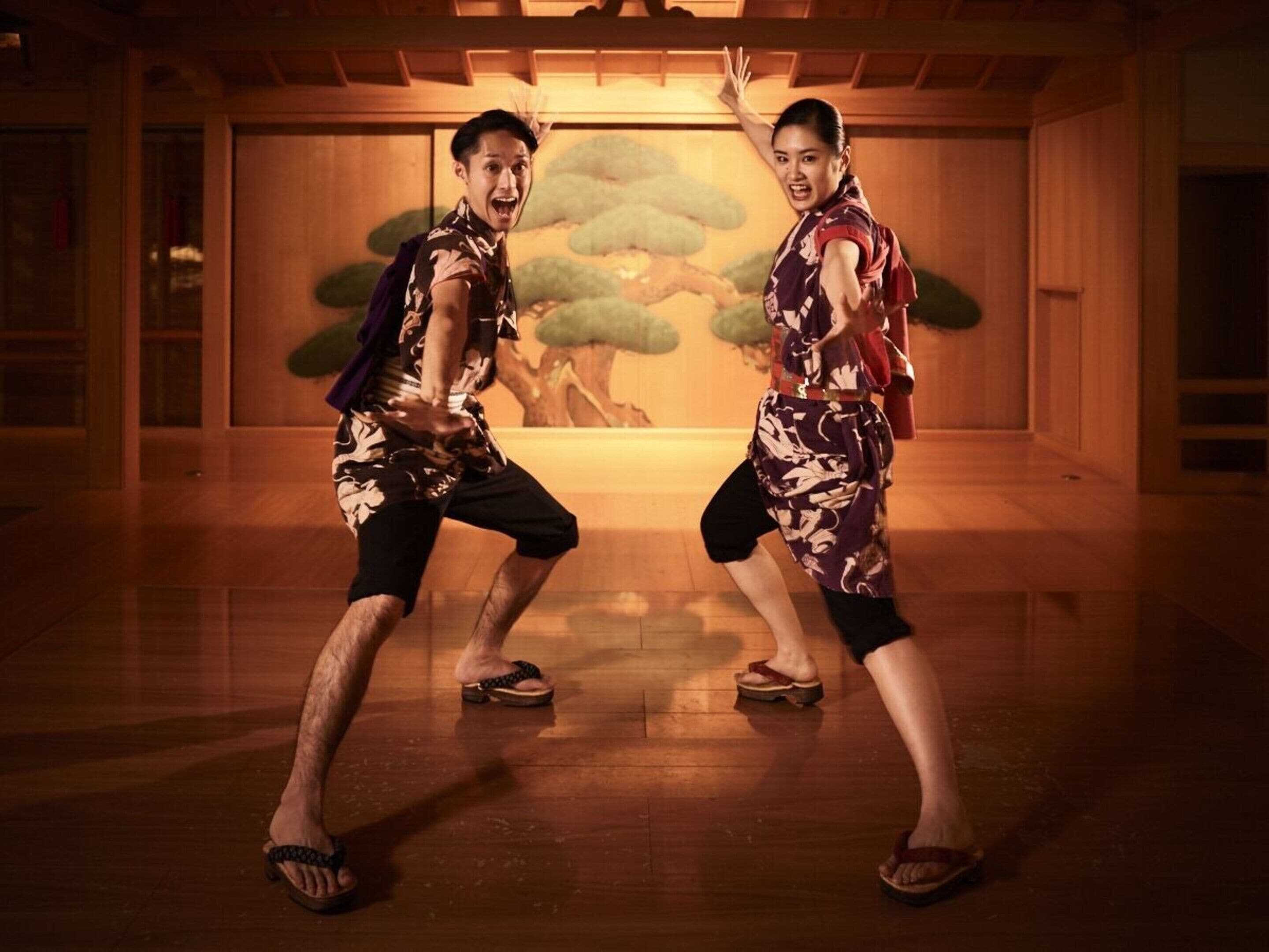 Two people in a room with wooden floors and a mural of trees.