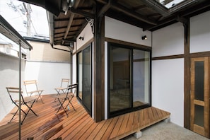 Terraza de madera con sillas, puerta corrediza de vidrio y un borde de hormigón.