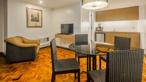 A modern living room with a glass dining table, black wicker chairs, a tan leather sofa, and a flat-screen TV. - Salcedo Suites (Makati)