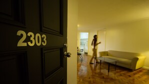 A room with a wooden parquet floor, a sofa, and a door with the number 2303. - Salcedo Suites (Makati)