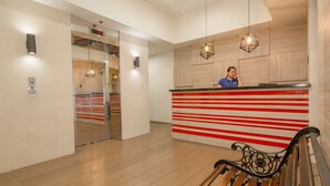 A reception area with a wooden bench, a receptionist, and a counter with red and white stripes. - Salcedo Suites (Makati)