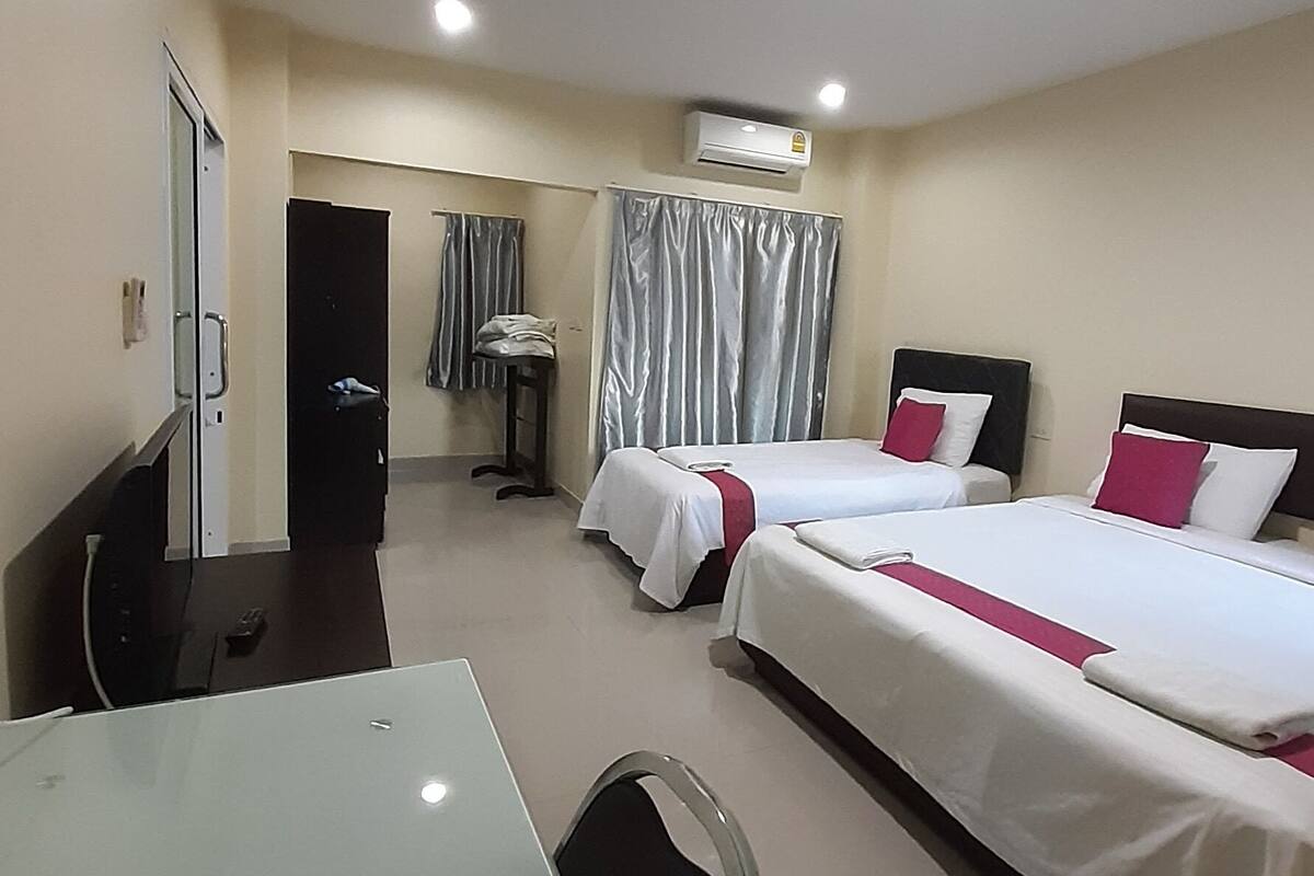 A hotel room with two beds, a desk, a chair, an air conditioning unit, and a door.