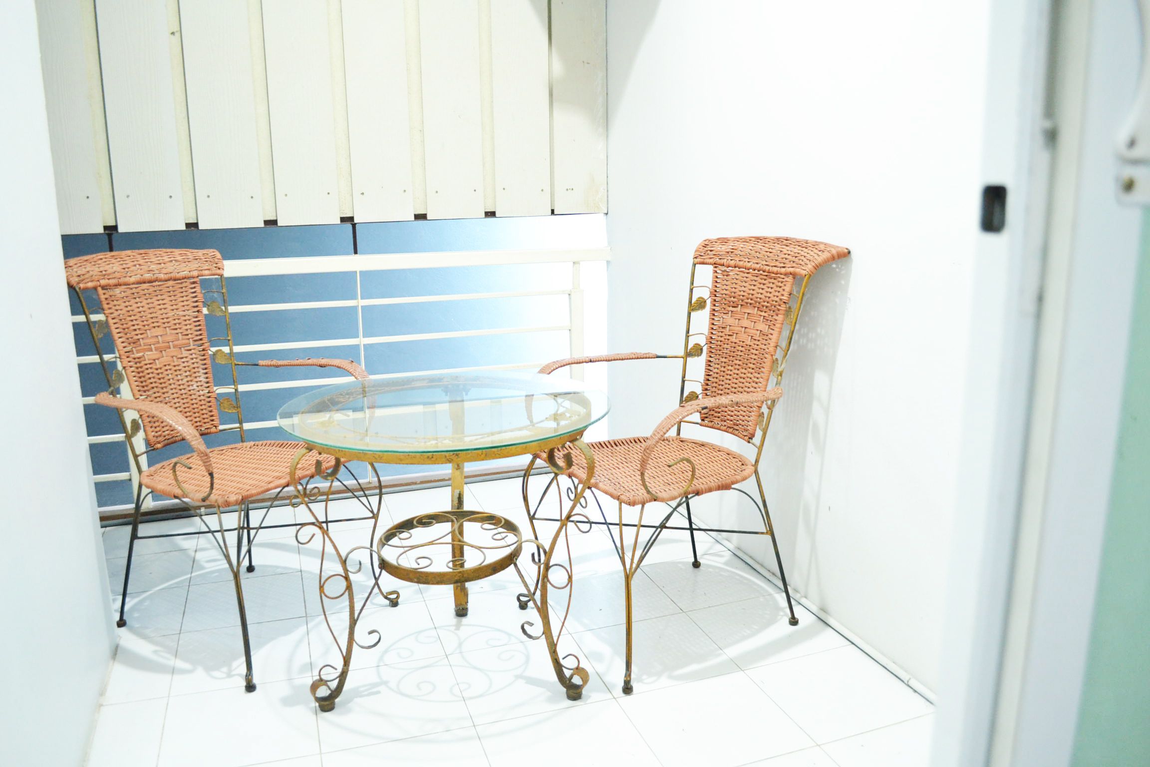 A small, enclosed outdoor area with a glass-top table and two wicker chairs.