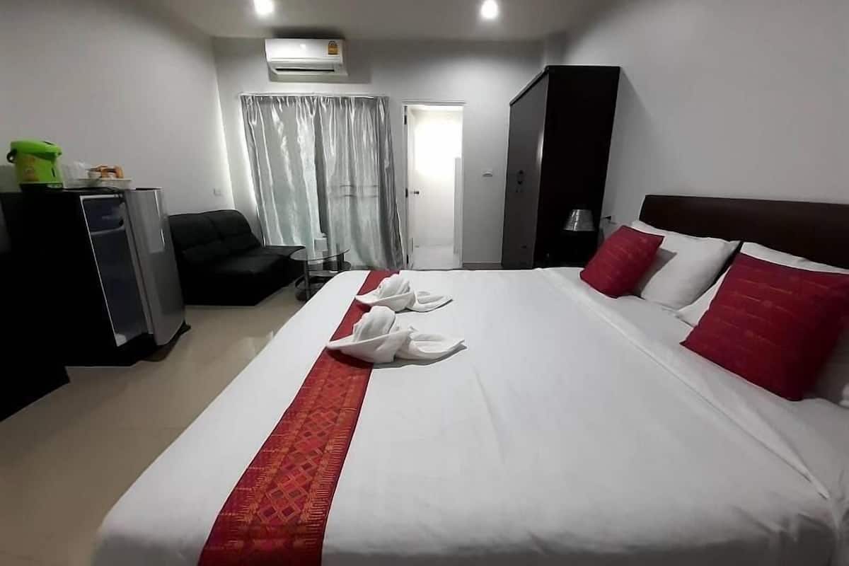 A hotel room with a bed, a desk, a chair, a wardrobe, and an air conditioning unit.