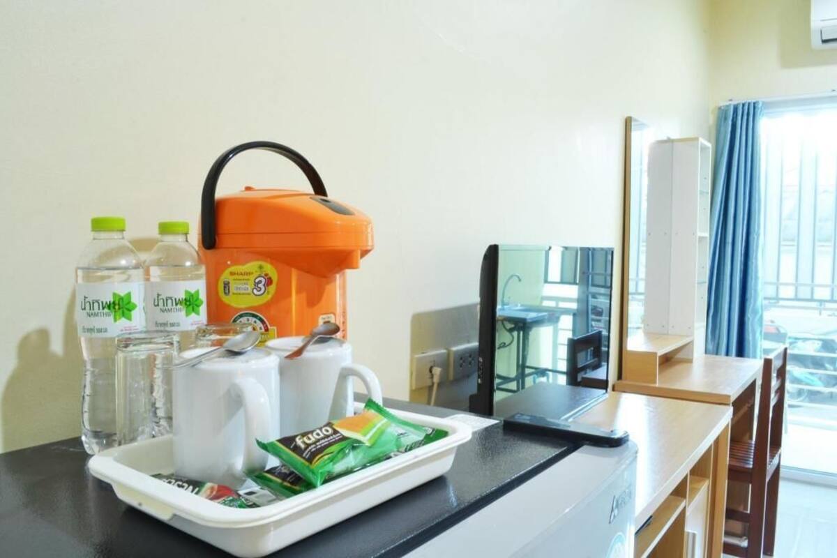 A hotel room with a table set with a water bottle, a mug, a juice box, a tray with snacks, and a portable coffee maker.