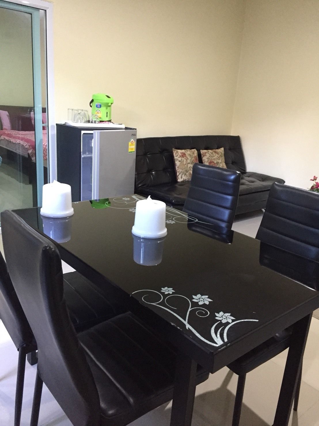 A dining table with four chairs, a refrigerator, a sofa, and a glass partition.