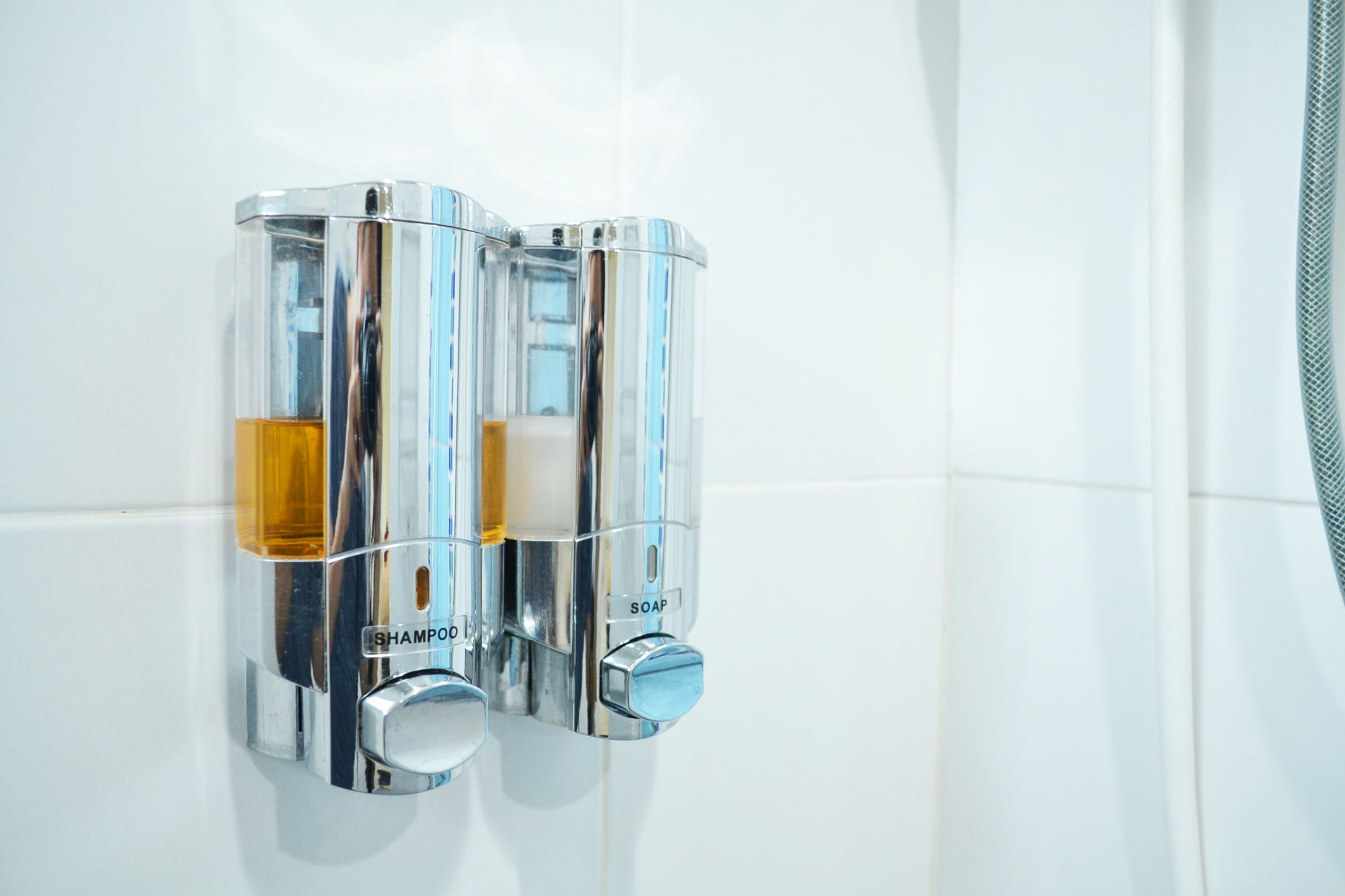 Een chromen zeepdispenser met een gele zeepstang en een blauwe zeepstang, voorzien van de tekst 