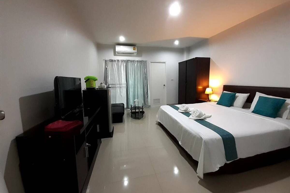 A hotel room with a bed, a desk, a television, an air conditioning unit, and a window with curtains.