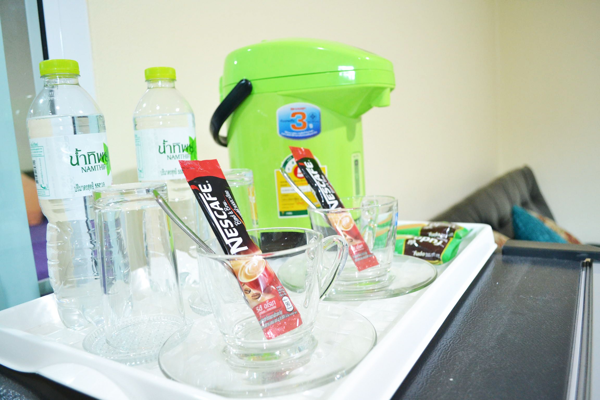 Un plateau avec des verres transparents, une bouteille d’eau verte et plusieurs emballages de boissons.