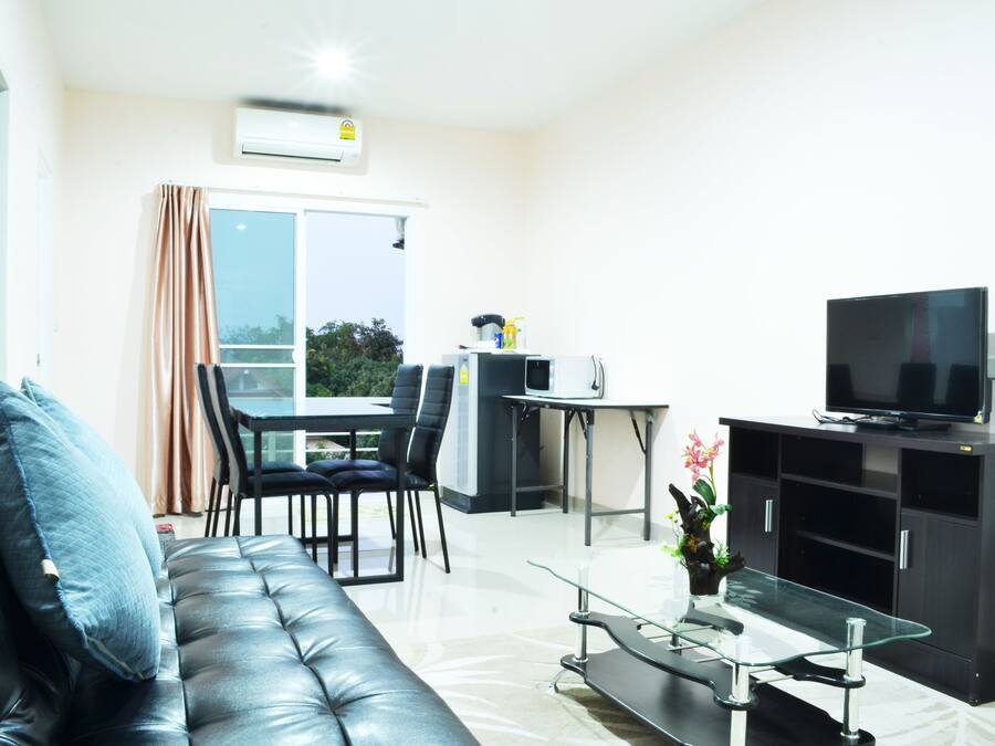 A modern living room with a leather sofa, a glass coffee table, a flat-screen TV on a black cabinet, and a dining area with a table and chairs.