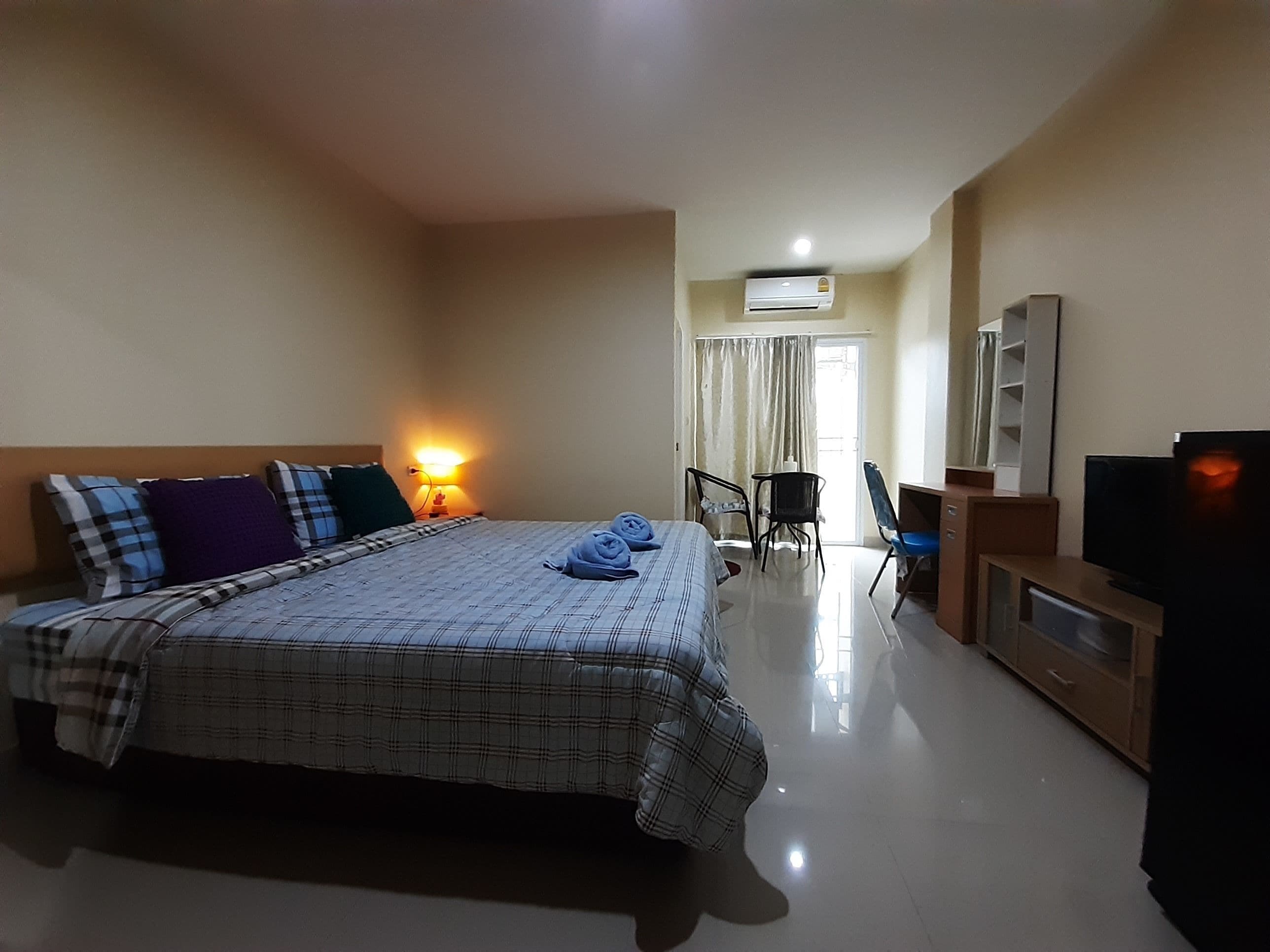A hotel room with a bed, a desk, a chair, a television, and an air conditioning unit.