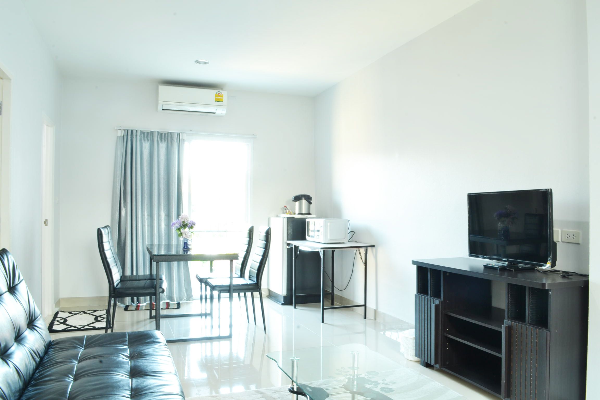 Una sala de estar moderna con un sofá, una mesa de comedor con sillas, un televisor de pantalla plana y una zona de kitchenette.