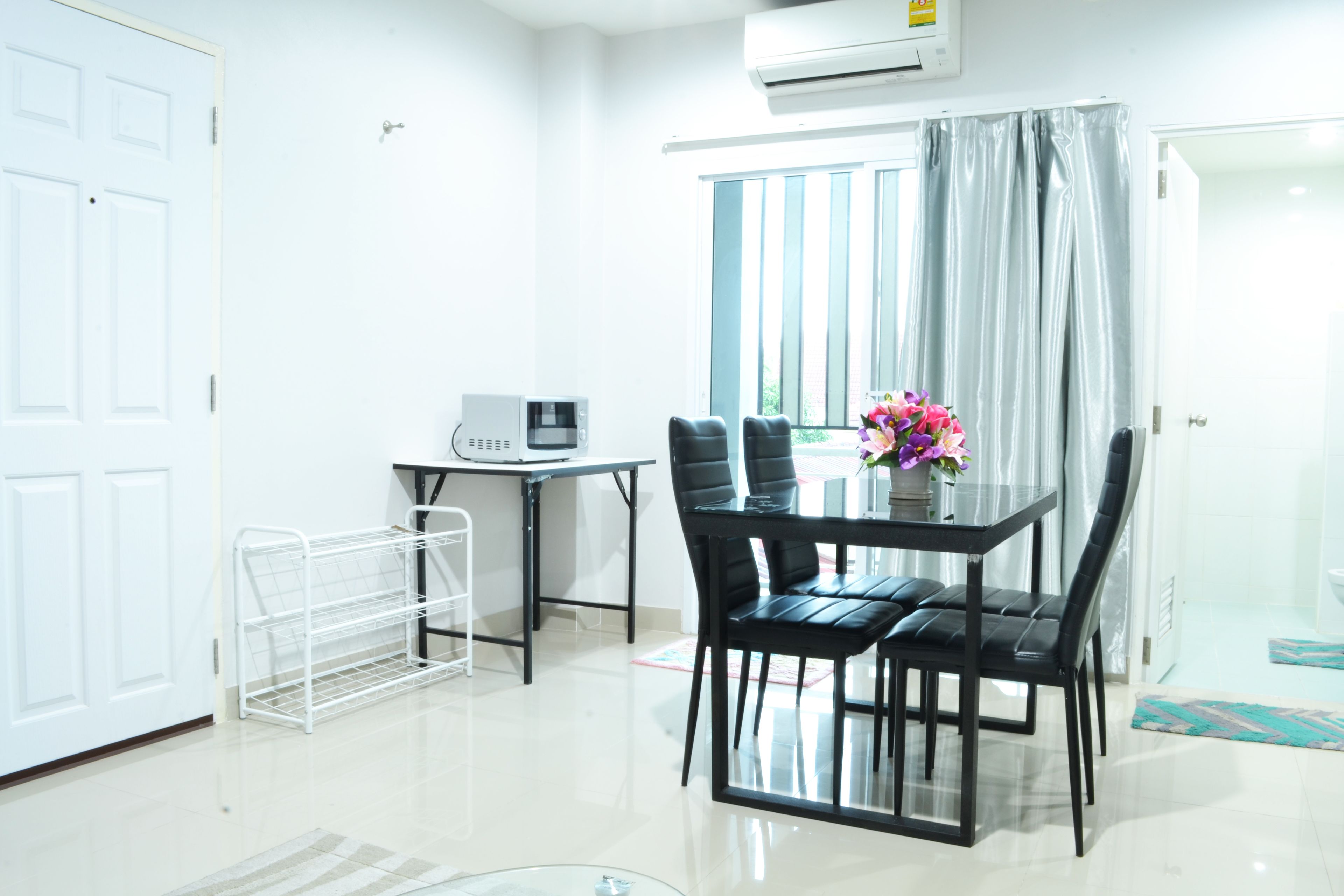 A modern room with a dining table, chairs, a small kitchenette, and a window with curtains.