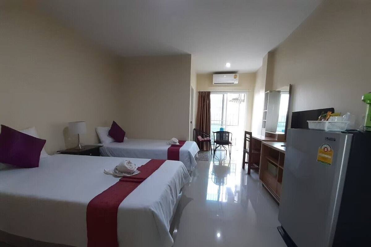 A hotel room with two beds, a desk, a refrigerator, and an air conditioning unit.