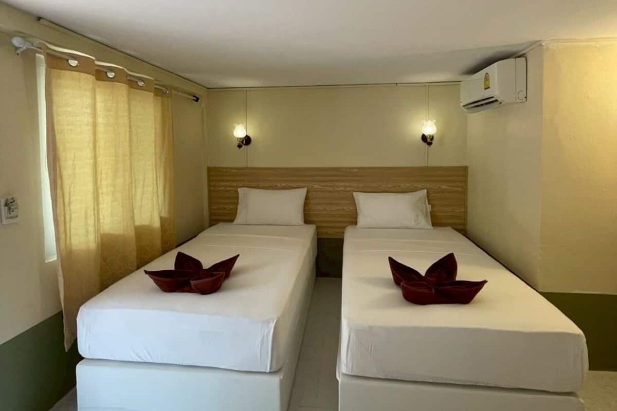 Una habitación de hotel con dos camas individuales, cabecero de madera, aire acondicionado de pared y ventana con cortinas.