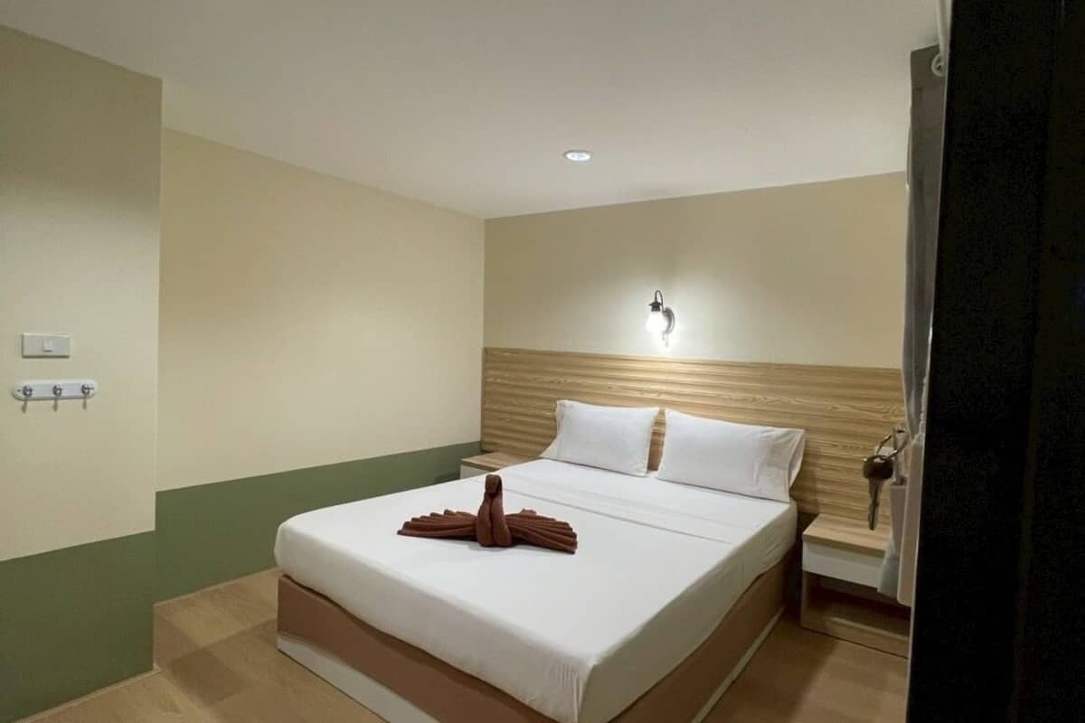 Habitación de hotel con una cama, una mesita de noche, una lámpara de pared y una lámpara en el techo.