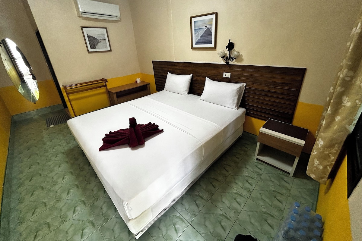 Habitación de hotel con cama, mesita de noche, equipo de aire acondicionado y un cuadro en la pared.