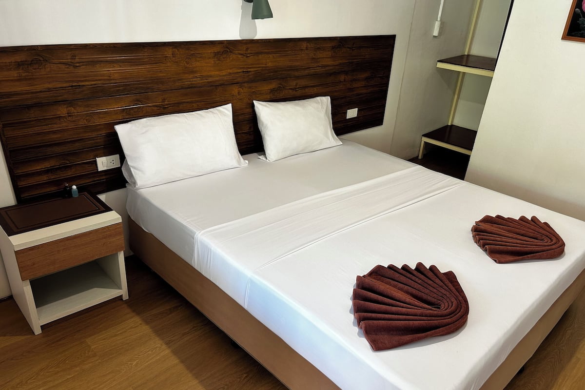 Una cama bien hecha con sábanas blancas y dos toallas marrones dobladas a un lado.