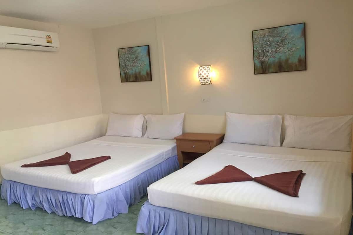 Habitación de hotel con dos camas individuales, cada una con una toalla marrón doblada encima. Hay una mesita de noche entre las camas, un aire acondicionado de pared y dos cuadros en la pared.