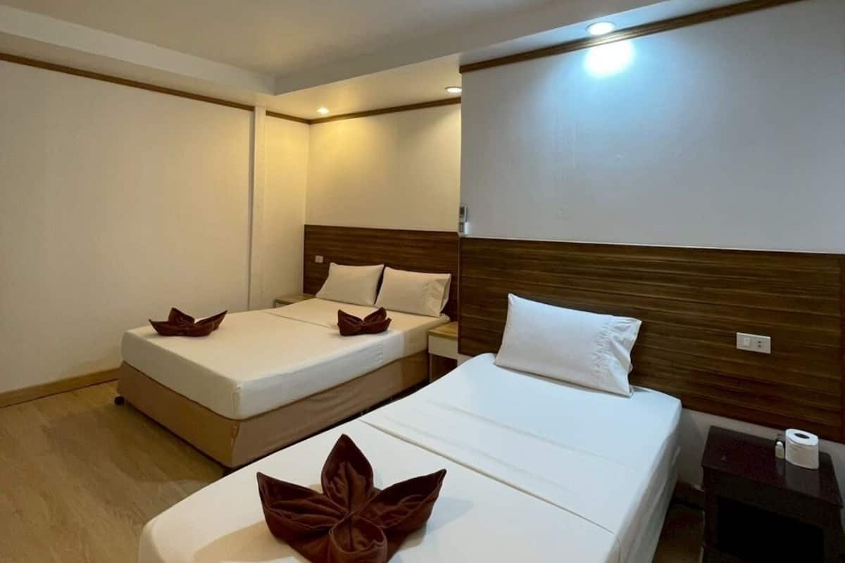 Habitación de hotel con dos camas individuales, cabecera de madera, mesita de noche pequeña con lámpara y luz en la pared.