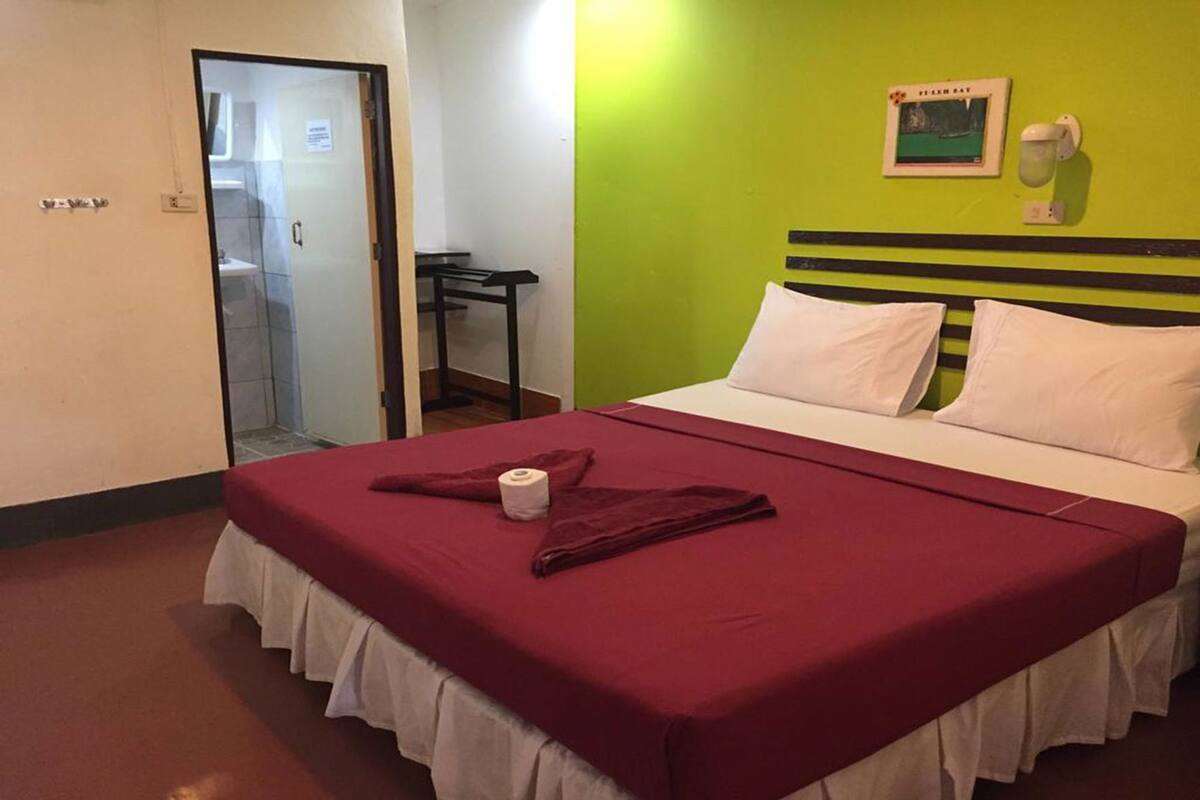 Habitación de hotel con cama, baño a la vista a través de una puerta abierta, una mesita y una lámpara fijada a la pared.