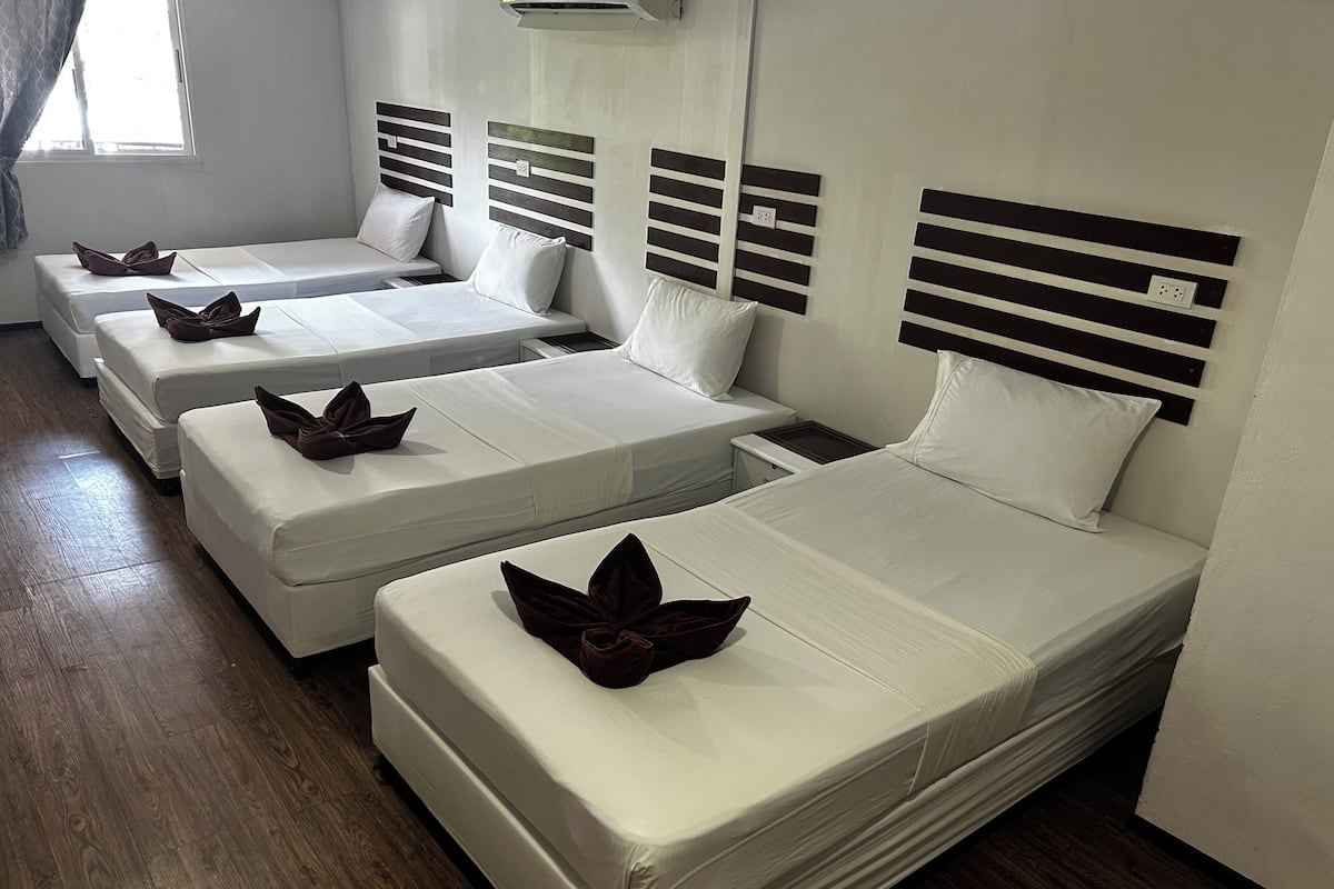 Habitación de hotel con cuatro camas individuales, cada una con cabecero de madera y colchón blanco.