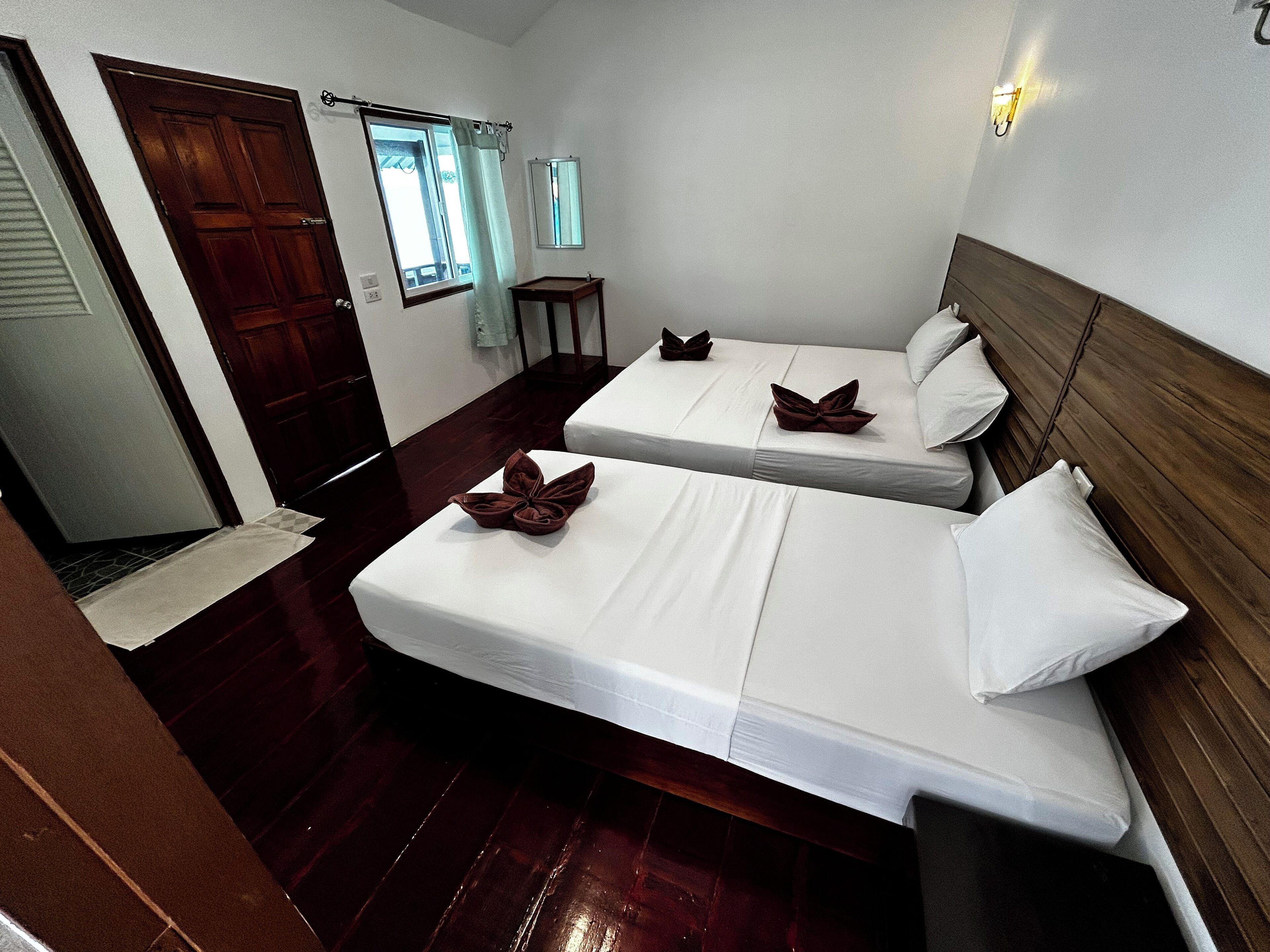 A hotel room with two beds, a wooden floor, a small table, and a window with curtains.