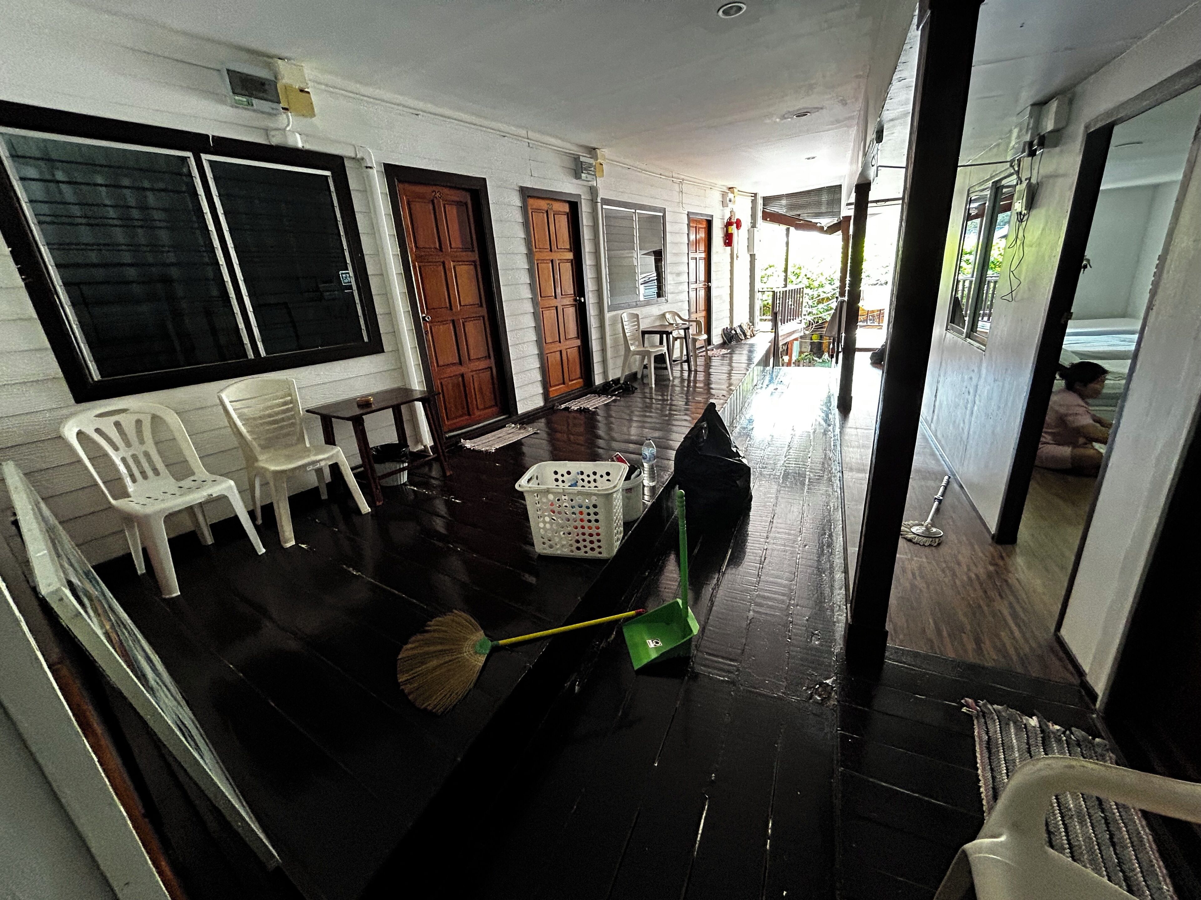 A room with a black floor, white walls, and wooden doors. There are plastic chairs, a table, and a green trash bin.